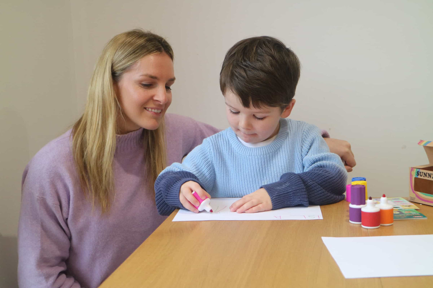 A woman supervising a child using a Sunny Marker to draw a picture on a piece of paper