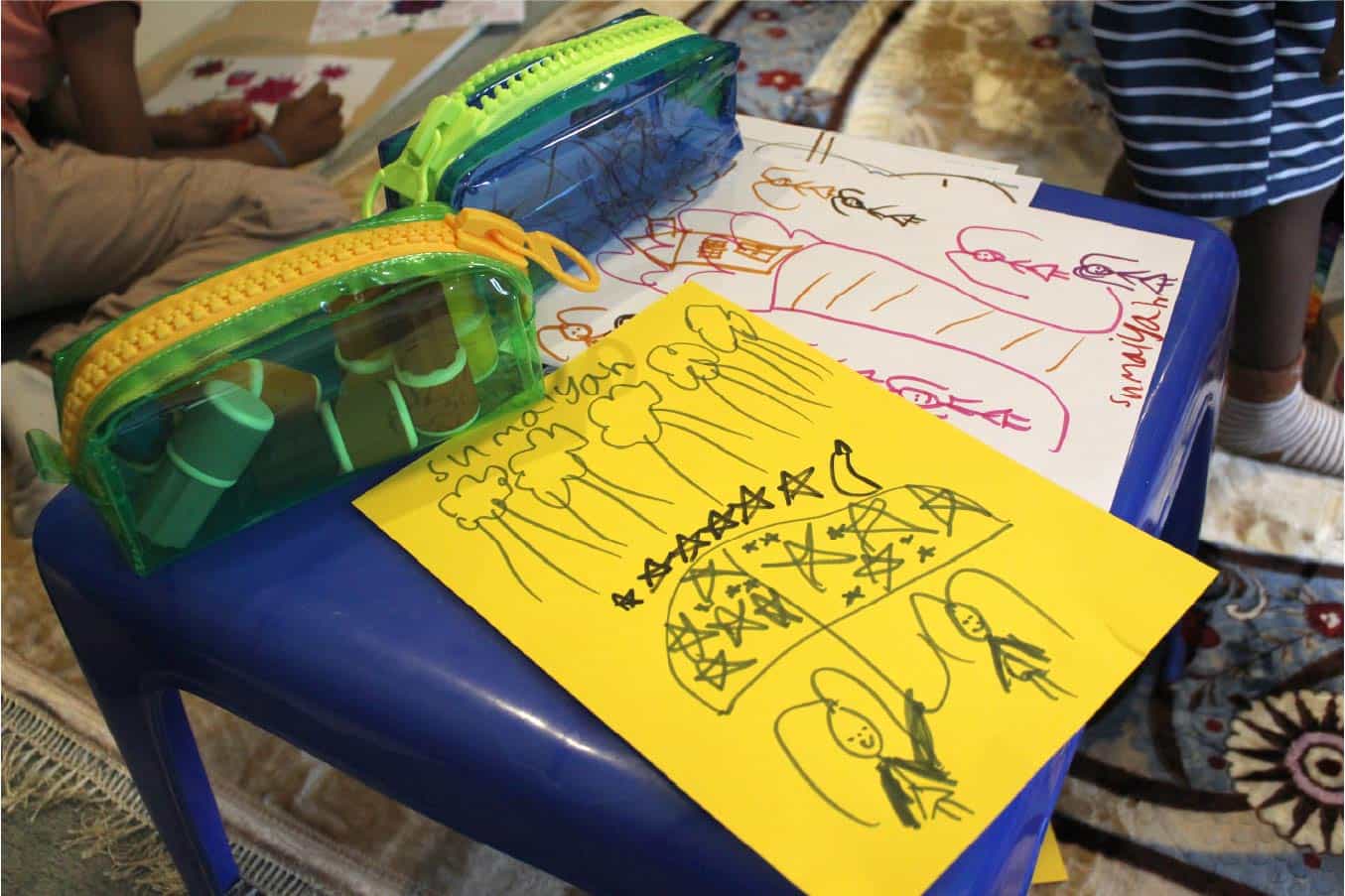 Two child's drawings alongside Sunny Markers inside of a pencil case