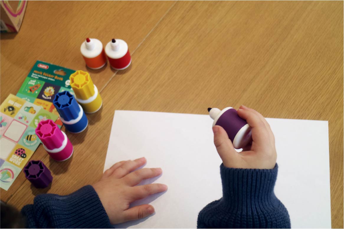 A child holding a Sunny Marker with a piece of paper and more Sunny Markers markers nearby